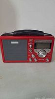 Front view of red portable radio with speaker on left, controls and display on right