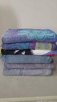Stack of six assorted towels in mixed colors and patterns, folded and stacked on a flat surface.