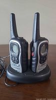 Two Uniden walkie talkies on black charging dock showing front and side views, including antennas, buttons, and display screens.