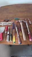 Various vintage hand tools laid out on a wood surface including pliers, hammers, screwdrivers, paint scraper