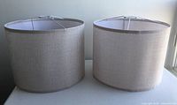 Two medium beige linen drum lamp shades placed side by side showing cylindrical shape and white spider fitter at top.