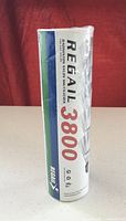 Front side of the sealed tube packaging showing 'Regail 3800 Badminton Nylon Shuttlecock' branding with white, blue, green, and red accents.