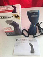 Photo showing the Black+Decker compact garment steamer with its box and user manual on a white surface, included brush attachment is visible.