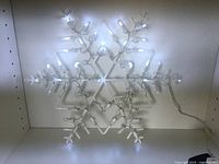 Lit snowflake shaped LED window silhouette light showing star design with white bulbs.