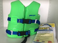 Front view of bright green Super Soft child size XS life jacket with blue adjustable straps and black clip buckle. Label 'SUPER-SOFT' visible on chest.