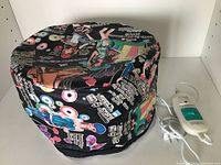 Electric thermal hair steamer bonnet showing colorful outer fabric with various designs and graphics, cap in upright position.