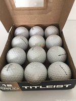 Open box showing 12 Titleist Pro V1 golf balls, white with dimples and markings.