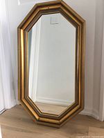 Vintage 22x38 inch octagonal wooden framed mirror standing against a wall with light wood flooring beneath. Gold finish visible with layered molding.