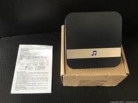 Wireless plug-in doorbell receiver unit on top of cardboard box with instruction sheet beside it.