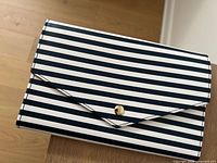 Closed view of ALDO travel wallet with navy and white horizontal stripes and gold-tone button snap.