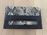 Photo of the front of the clutch bag showing the snakeskin print flap with black faux leather body.