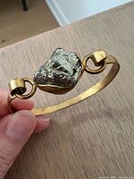 Gold-tone brass hinged bangle bracelet with rough pyrite stone centerpiece held in hand showing size and detail.