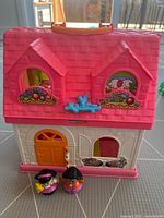 Exterior view of Fisher-Price Little People house showing pink roof, white walls with decorative stickers, and two figures placed in front.