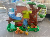 Overall front view of the Fisher-Price Little People zoo playset including the tree structure, slide feature, and three animal figures positioned in front.