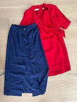 Red silk dress and navy blue silk skirt laid flat on wooden floor, showing full view of both garments.