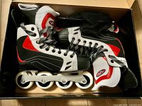 Top view of the rollerblades inside original box showing black, white, and red boots with laces and wheels.