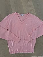 Full view of light pink V-neck acrylic sweater laid flat on wooden floor