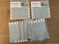 Five full sheets and twelve partial sheets of sea glass peel and stick backsplash tiles on wooden floor.