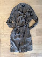 Full view of the taupe trench coat laid flat on wooden floor showing the overall design and belt.