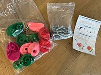 Set of 12 climbing holds in green, pink, and red with bag of mounting bolts and installation instruction sheet laid out on wood floor.