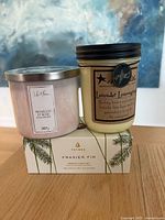 Photo showing three candles: Prosecco Et Rosé scented candle in pink wax in glass jar with silver lid, Lavender Lemongrass candle in amber jar with black screw lid and charm, and Thymes Frasier Fir candle boxed set