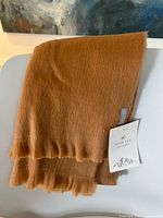 Photo of the caramel brown scarf with a Pokoloko tag and fringe edges laid flat on a chair.