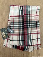 Folded wool scarf showing plaid pattern in cream, red, black, and beige with brand and hang tags.
