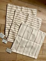 Three beige and white striped cushion covers laid out showing different stripe patterns and sizes.