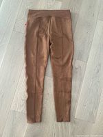 Full view of caramel-colored faux suede leggings laid flat, showing the front with seam detailing and wide waistband.