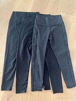 Three black leggings laid out flat to show the full length and high waistband. The leggings appear new without tags.