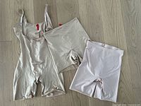 Set of 3 Spanx shapewear pieces: one bodysuit and two pairs of shorts laid out on floor
