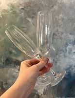 Two glass champagne flutes being held, showing clear, tall and slender design with long stems.