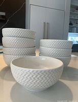 Stacked and arranged view of eight white bowls showing textured chevron exterior sides and one bowl facing down to show interior.