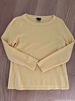 Front view of the pastel yellow sweater laid flat on a wooden floor showing long sleeves and crew neck