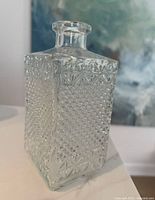 Front side view of square pressed glass decanter showing detailed diamond and star-like patterns on clear glass.