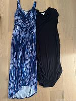 Two women's dresses laid flat on wooden floor. Left dress sleeveless with multicolor blue-purple-black pattern by Tommy Bahama, size small. Right dress short sleeve black by Fourteenth Place, size small.