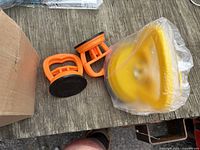 Two orange suction cup dent pullers and sealed yellow foam polishing pad on tabletop