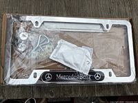 Two chrome Mercedes-Benz license plate frames in original packaging with mounting hardware visible