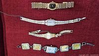 Four ladies watches on red fabric: gold/black Seiko, silver-gold rectangular Seiko, gold/white Seiko, map panel bracelet watch