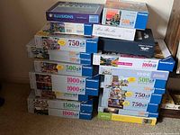 Stack of boxed jigsaw puzzles showing Ravensburger 500-1000 piece titles and other brands