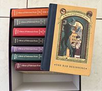 Front cover of The Bad Beginning resting atop stack of other series books in box