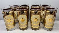 Front angled view of all eight Libbey highball glasses showing gold sunburst and medallion design