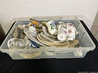 Plastic bin with assorted china including cups, saucers, and plates showing various designs and floral patterns.