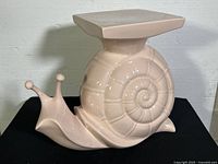 Side view of light pink ceramic snail plant stand showing shell detail and antennae, with one antenna repaired.