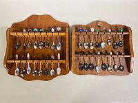 Full front view of two wooden racks displaying 32 collector teaspoons with various enamel crests on handles