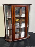 Front view of wood display case showing curved glass sides and mirrored back behind two folding shelves.