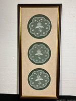 Full view of the vertical wood frame housing three round Carrickmacross lace pieces on a beige matte with glass cover.