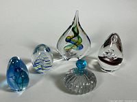 Five glass art pieces of varying shapes and internal designs displayed together on a flat surface.