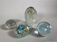 Four glass paperweight art pieces displayed together, showing range of sizes and colors