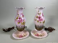 Pair of pink hurricane style table lamps with floral painted glass bases and shades, with power cords included.